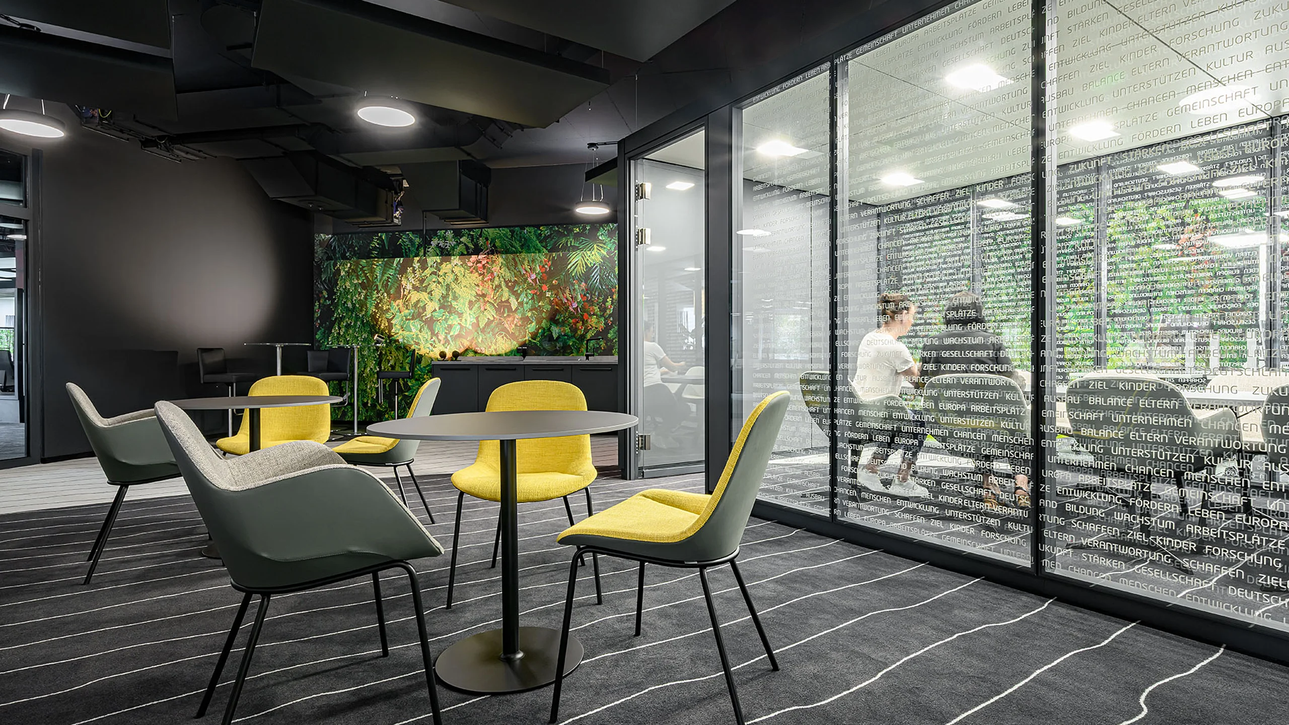 A meeting room featuring a T35 glass partition system and decorative vinyl lettering. In the foreground stands a small meeting table with colorful seating.
